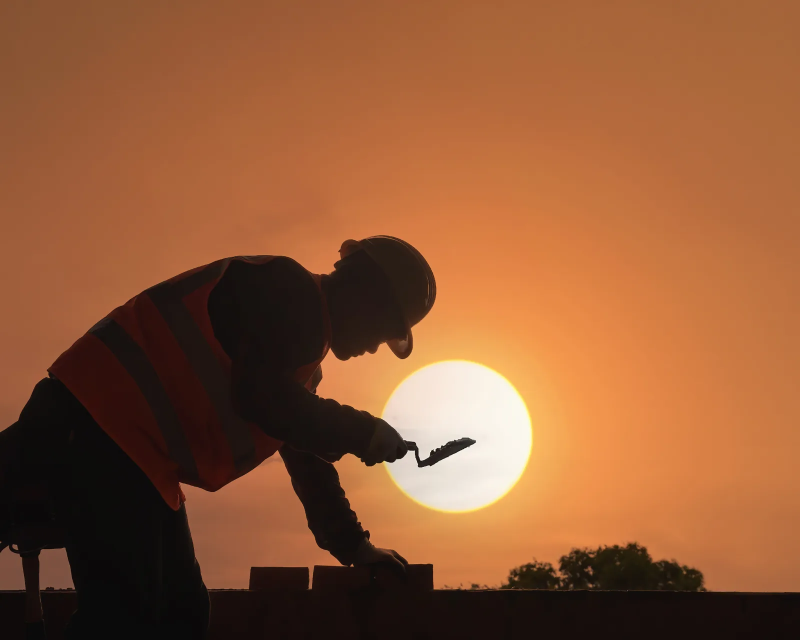 A mason laying brick against the setting sun